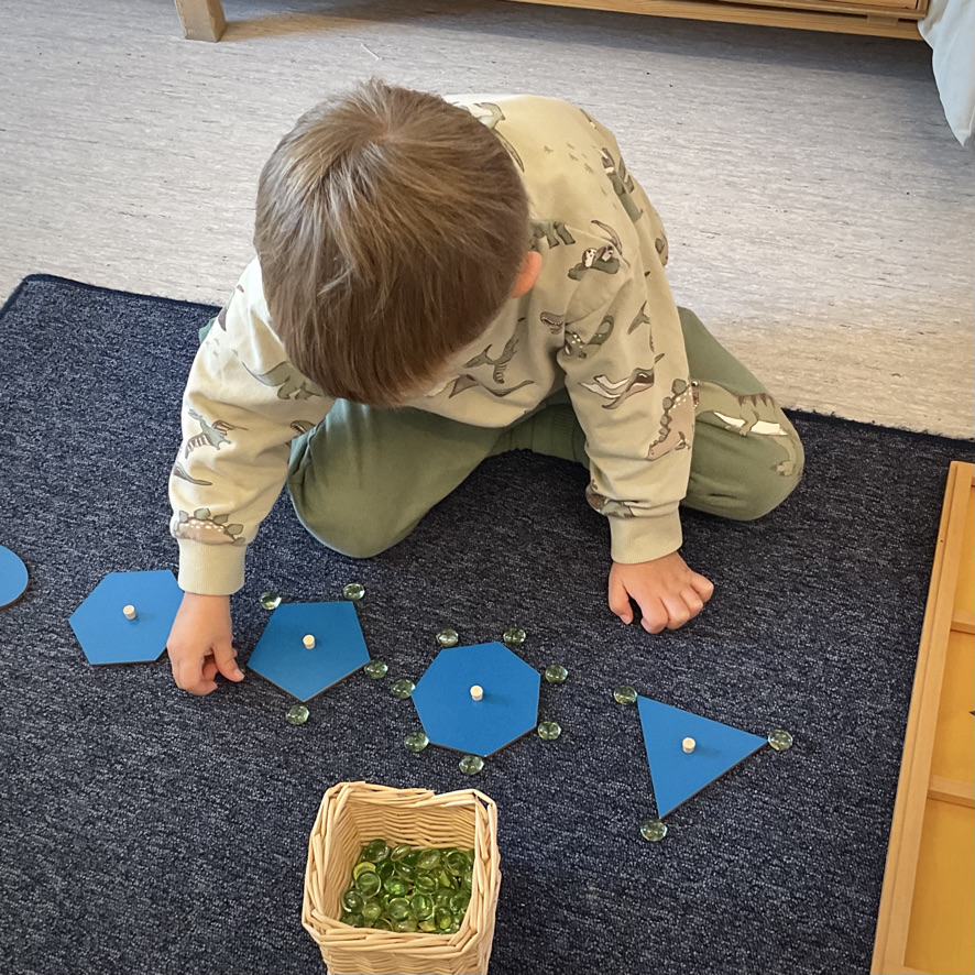 Barnet arbetar med blå geometriska former på en arbetsmatta.